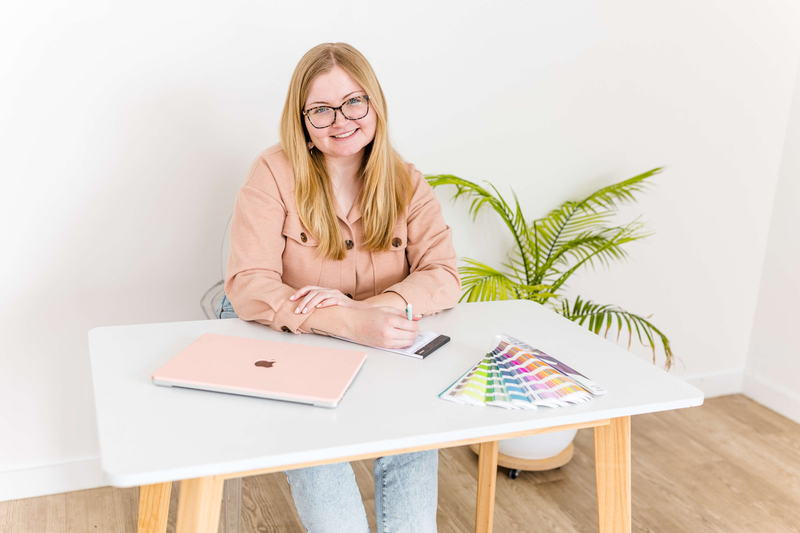 personal branding for creative entrepreneurs woman with blonde hair sitting at table with pantone swatches and pink laptop