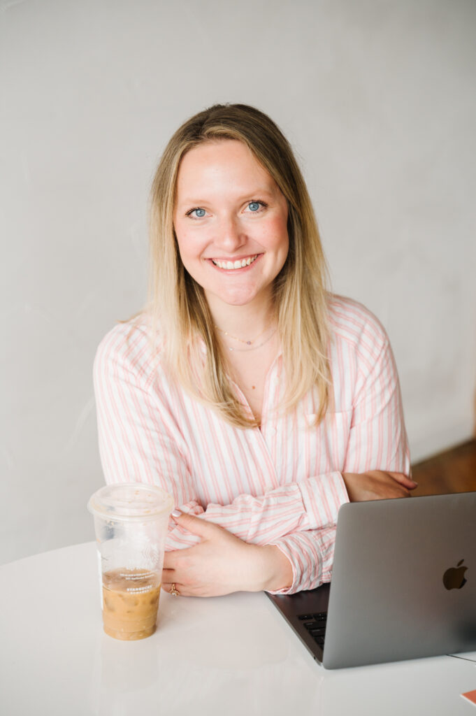 Woman smiling at camera sitting at table with laptop wearing light pink top