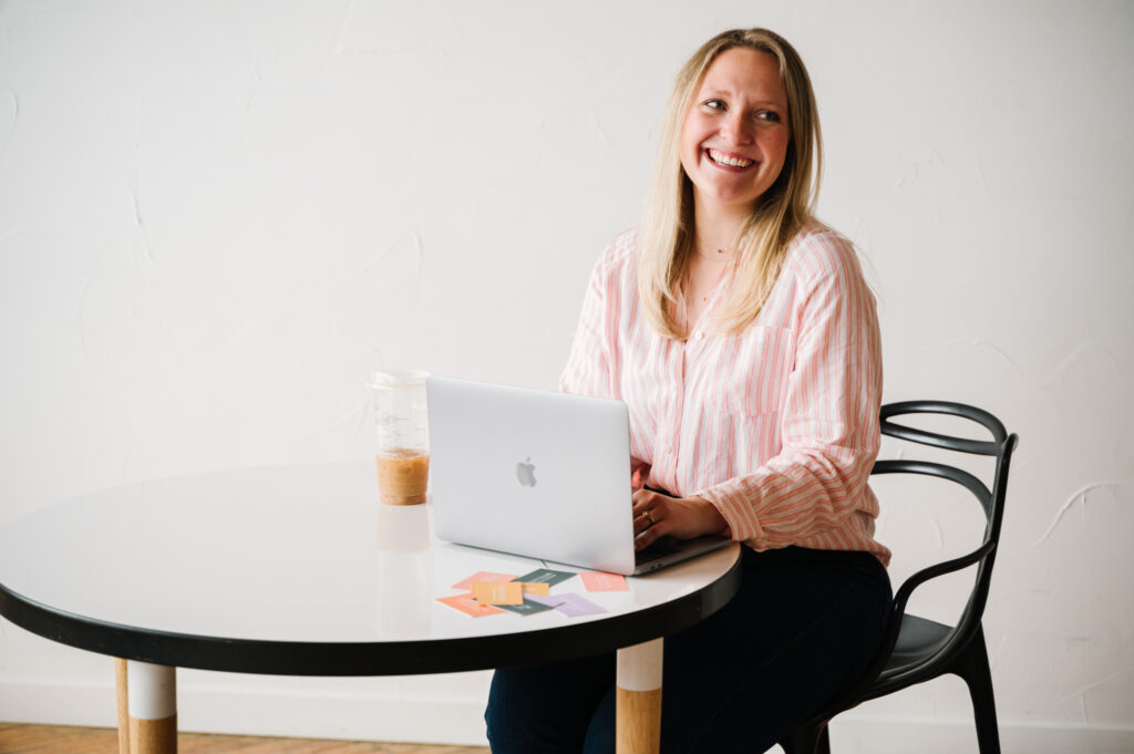 woman with blonde hair smiling as she sits at table with laptop