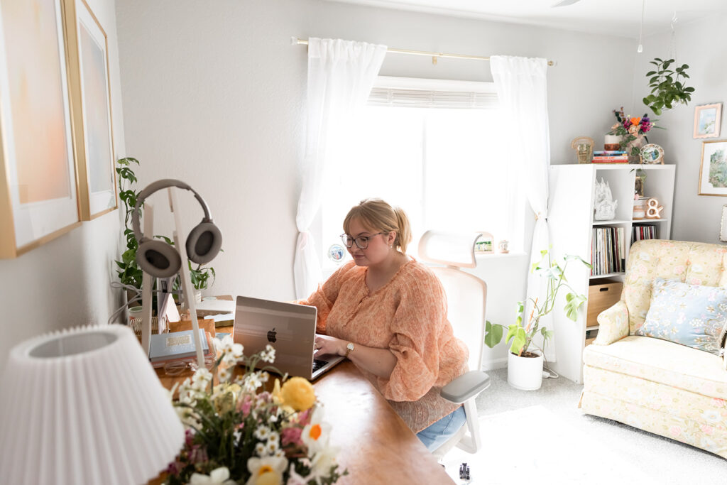 Woman with blonde hair wearing pink blouse sitting at desk in brightly lit office