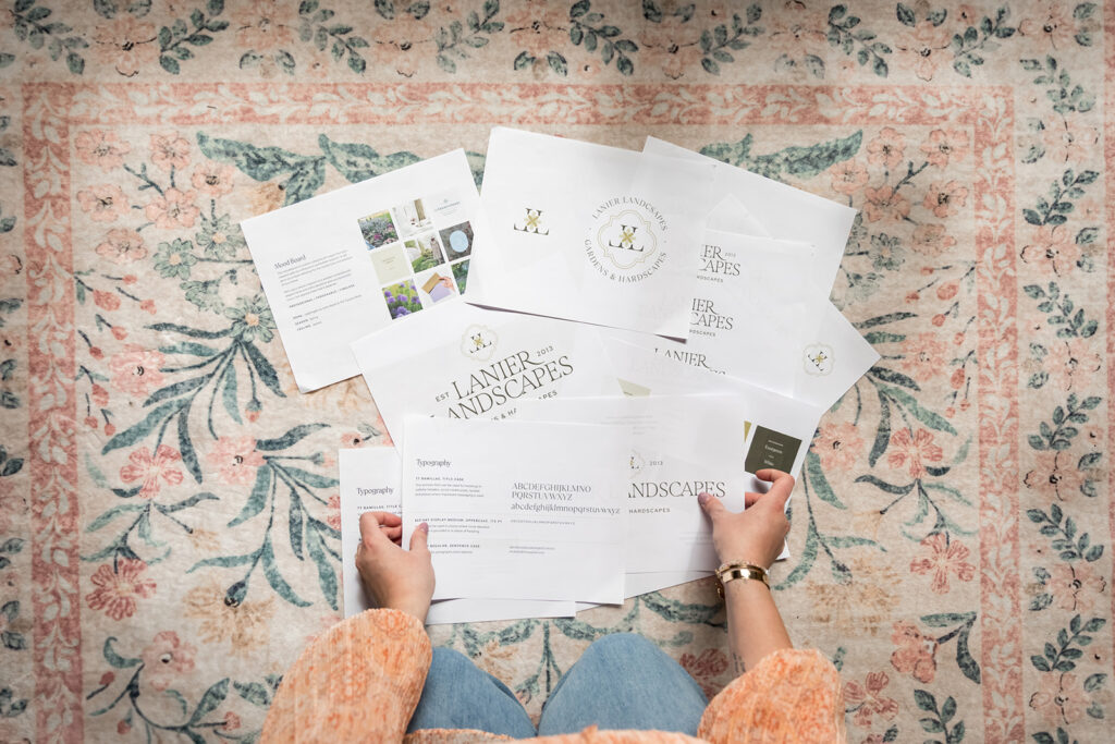 Woman's hands sorting through printed out papers of brand identity whimsical design for Lanier Landscapes sitting on floral rug