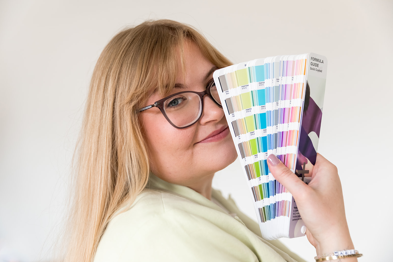 woman with blonde hair and glasses covering face with pantone swatch book